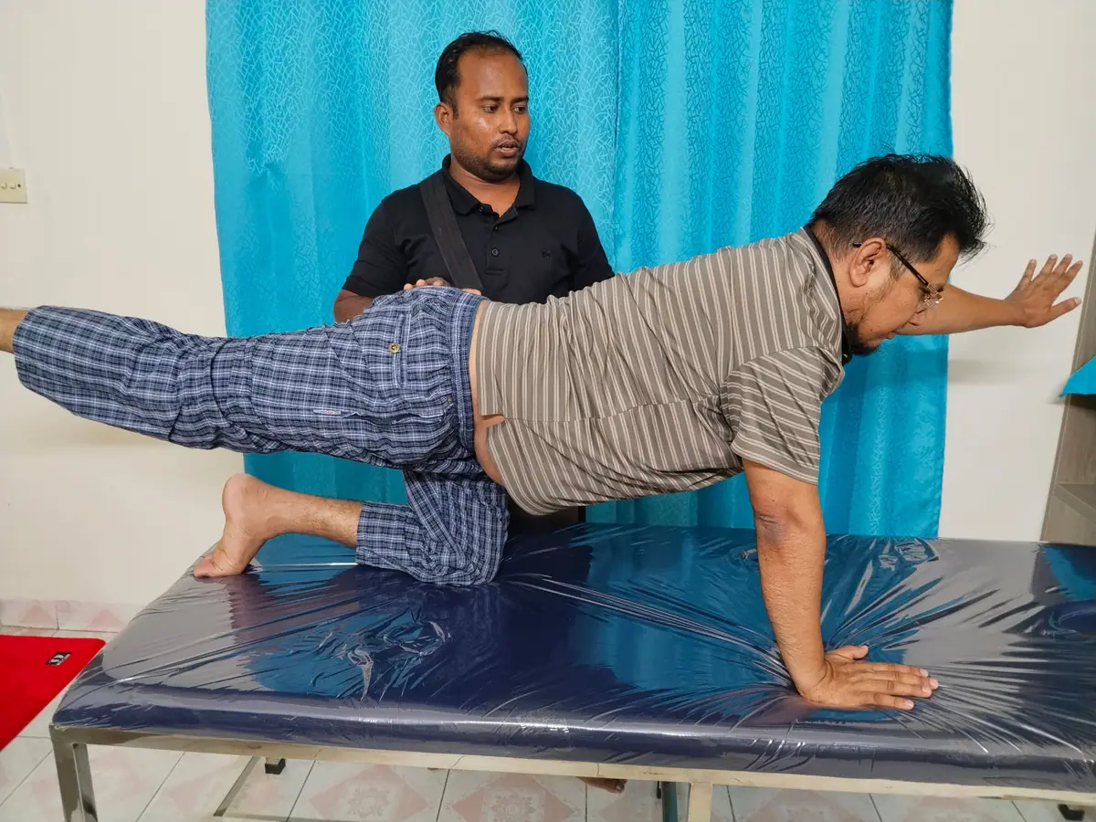 A physiotherapist supporting a patient through a controlled core stability exercise on a treatment couch at Physio Motion