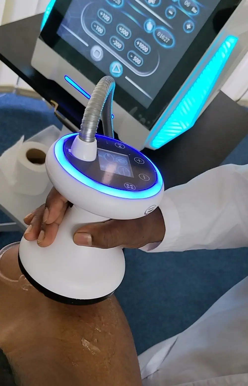 A physiotherapist applying a focused shockwave therapy applicator to a patient’s knee, with the treatment console behind
