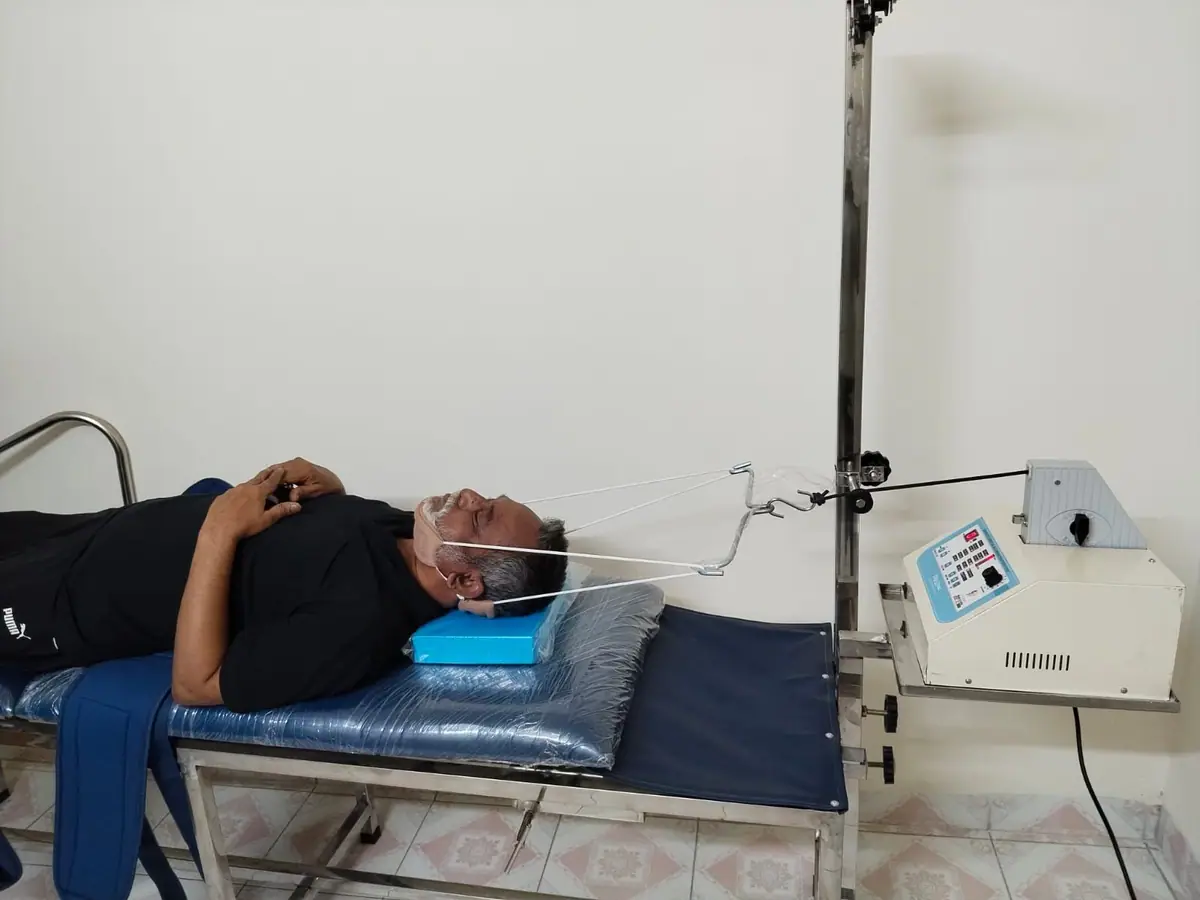 A patient lying down receiving cervical traction through a head harness connected to a traction unit